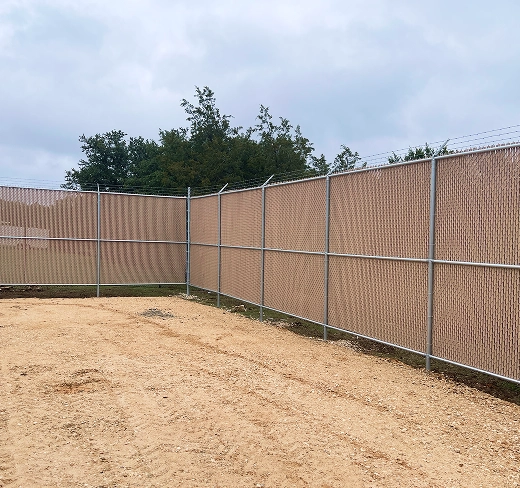 A tall tan vinyl privacy chain-link fence bordering construction site.