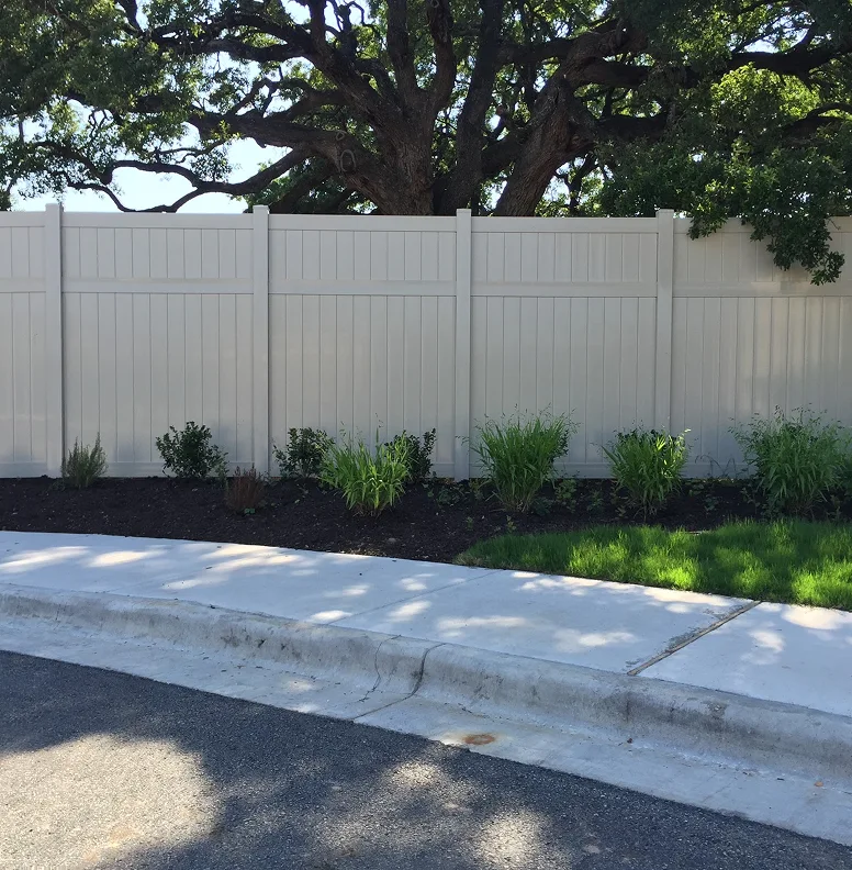Cream colored vinyl fence along mulch bed and side walk in residential neighborhood.
