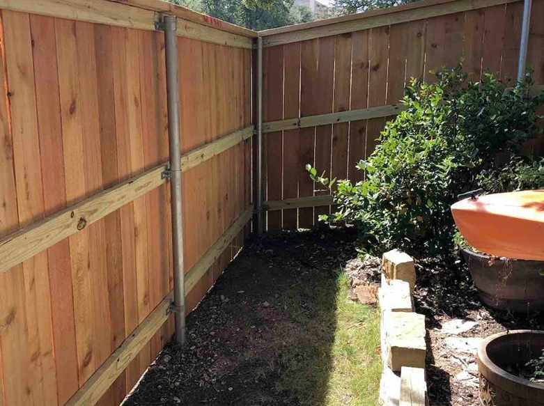 An interior view of a dog-ear cedar privacy fence corner supported by galvanized steel posts and horizontal wood rails.